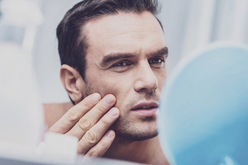 man examining face in mirror, touching cheeks.