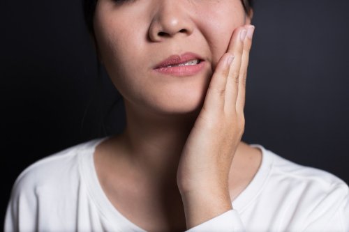 woman holds aching jaw.