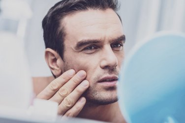man examining face in mirror, touching cheeks.