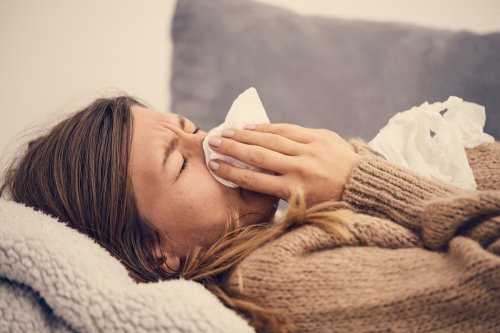 woman in bed blowing nose with tissue.