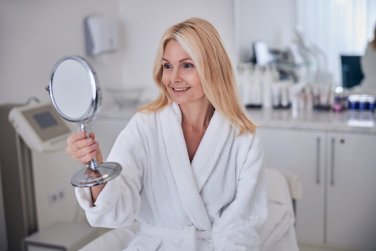 woman holds handheld mirror in hand in medical spa.